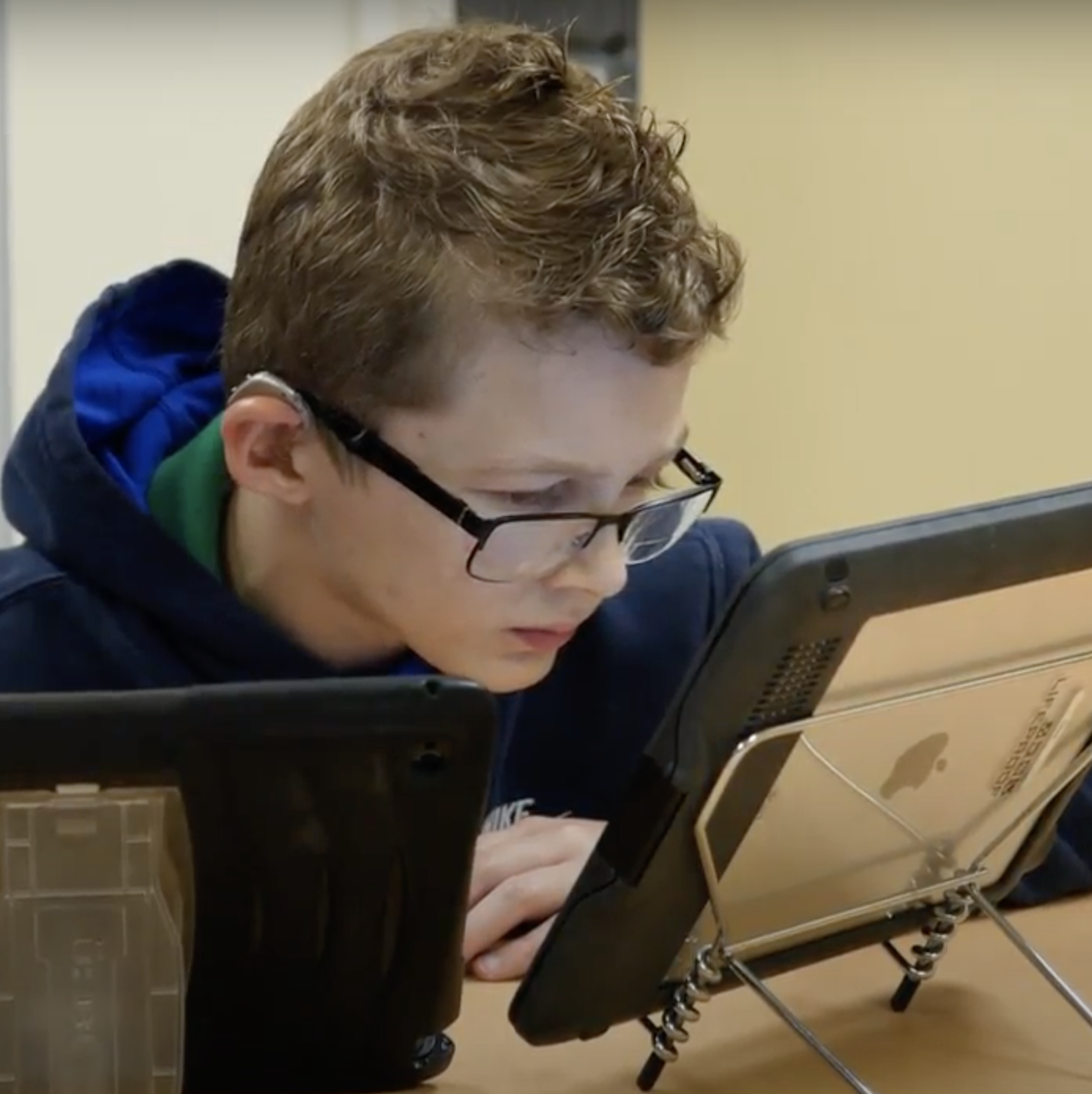 A boy with glasses and hearing aids looking at an iPad