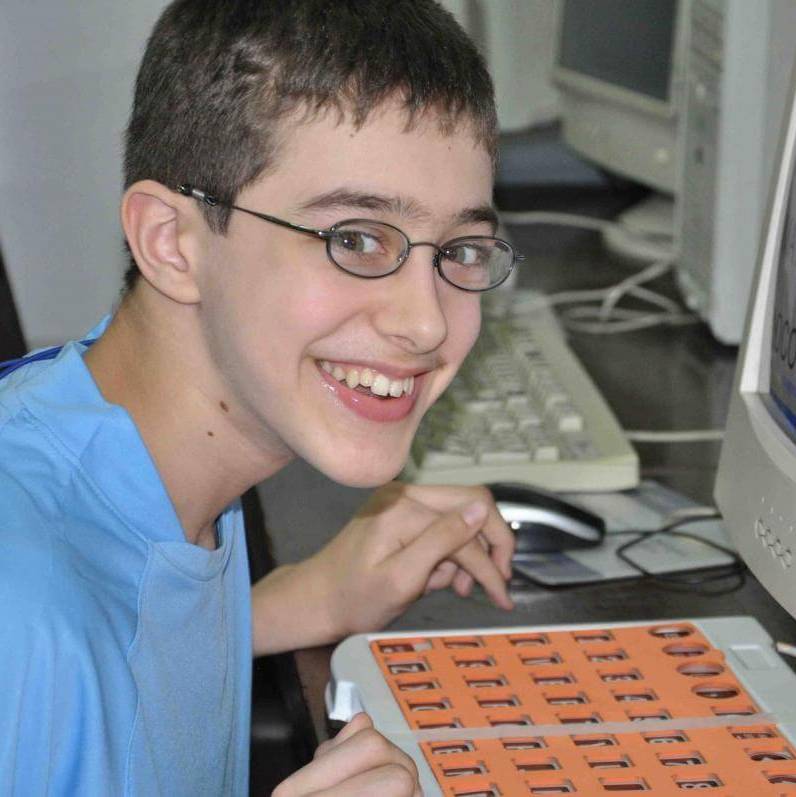 A boy with glasses uses an adapted keyboard and enlarged text on a computer screen