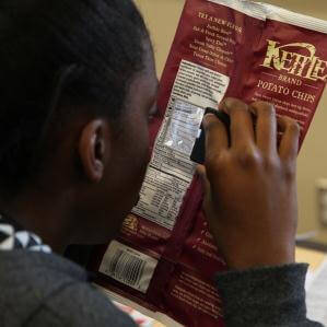 A girl uses a hand-held magnifier to read the nutritional information on a bag of potato chips.
