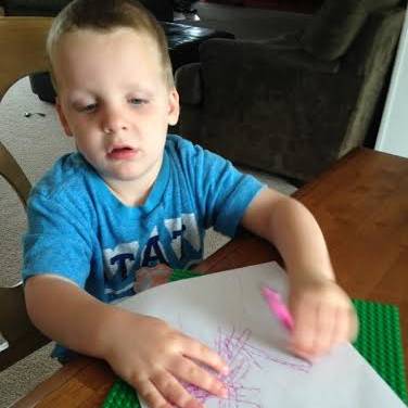 A young boy draws with a crayon on a paper on a textured surface