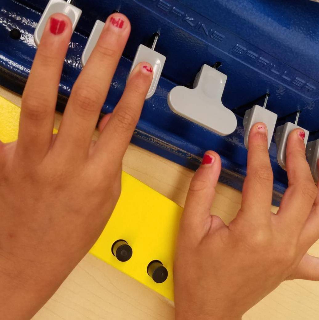 A young girl’s hands on the keys of a braillewriter with an open swing cell in the foreground.