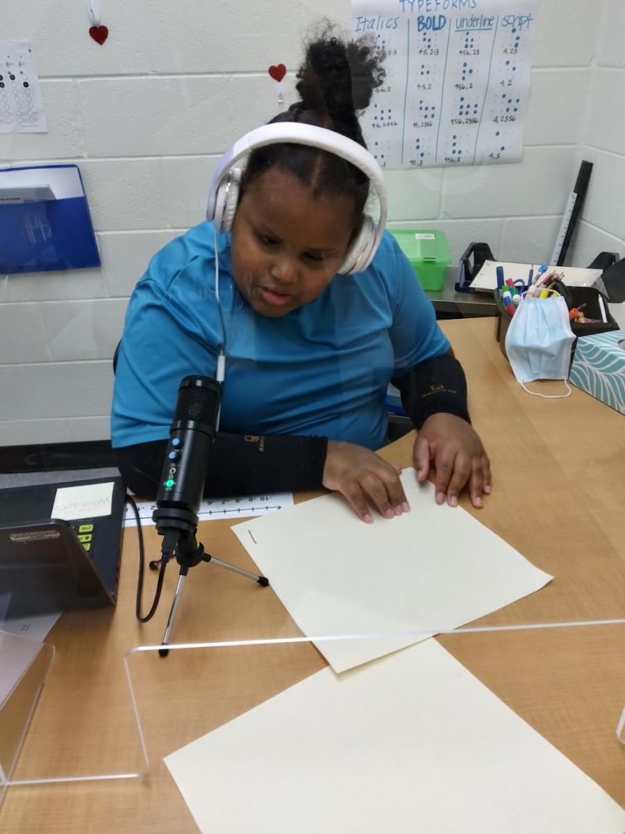 A girl wearing headphones reads a braille paper