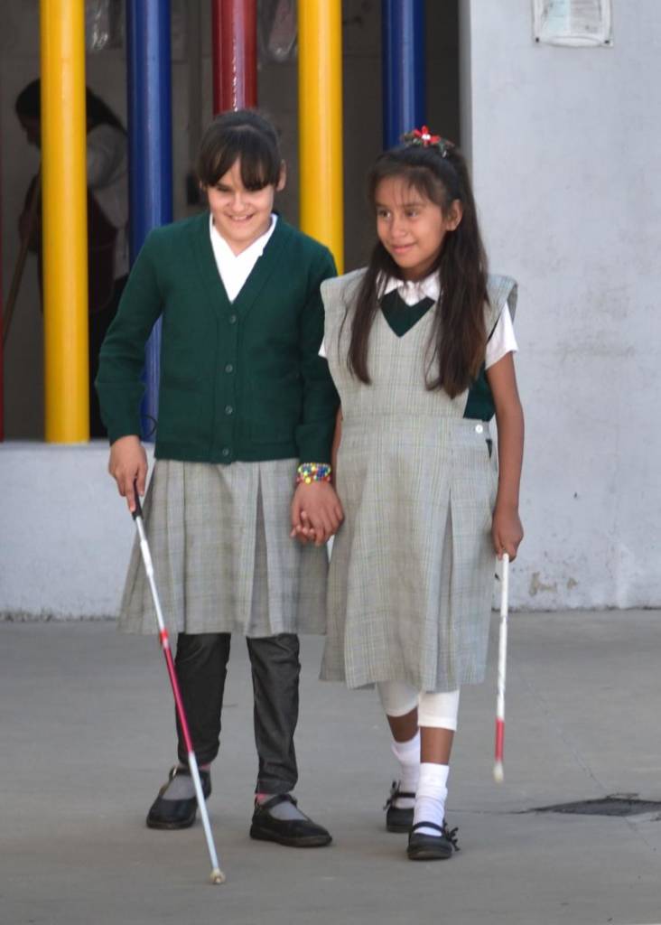 Two girls hold hands while also holding long canes
