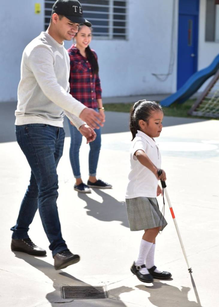 A man follows a young girl using a long cane