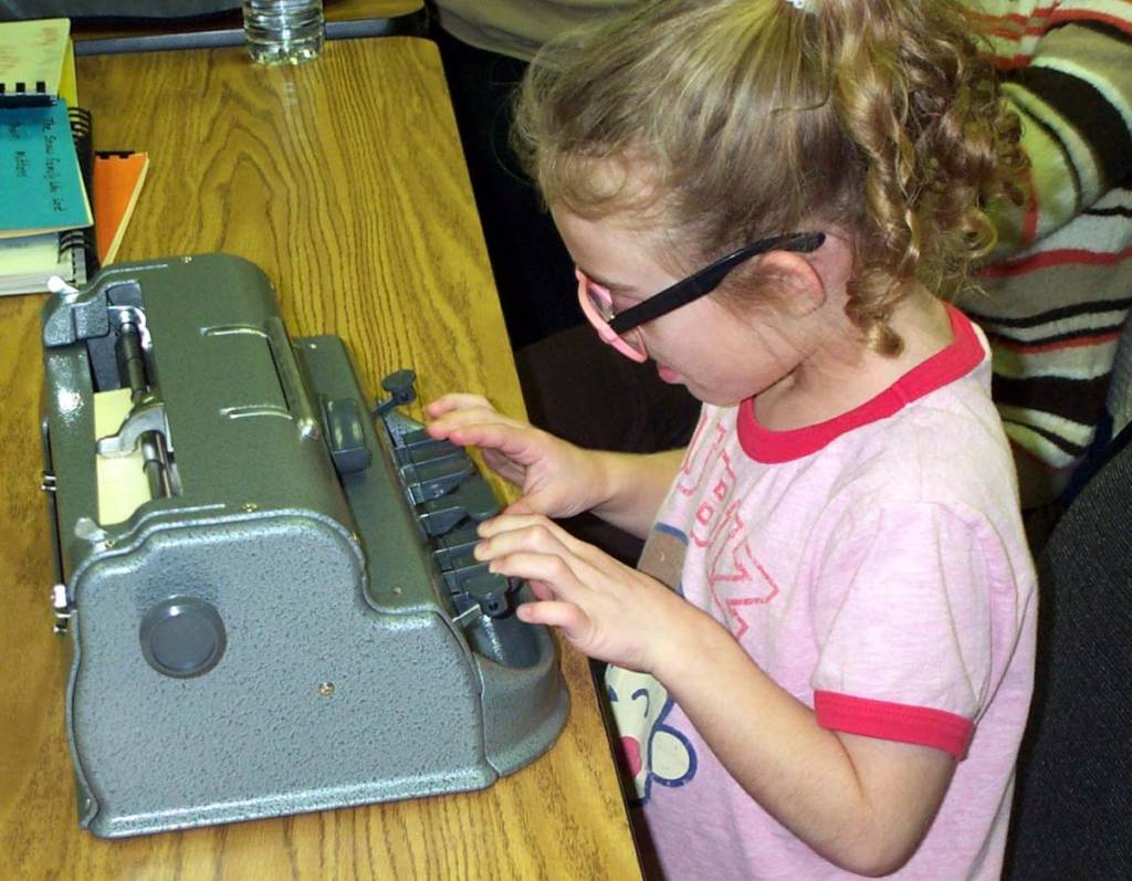 A young girl in a pink shirt is using a Perkins Brailler.