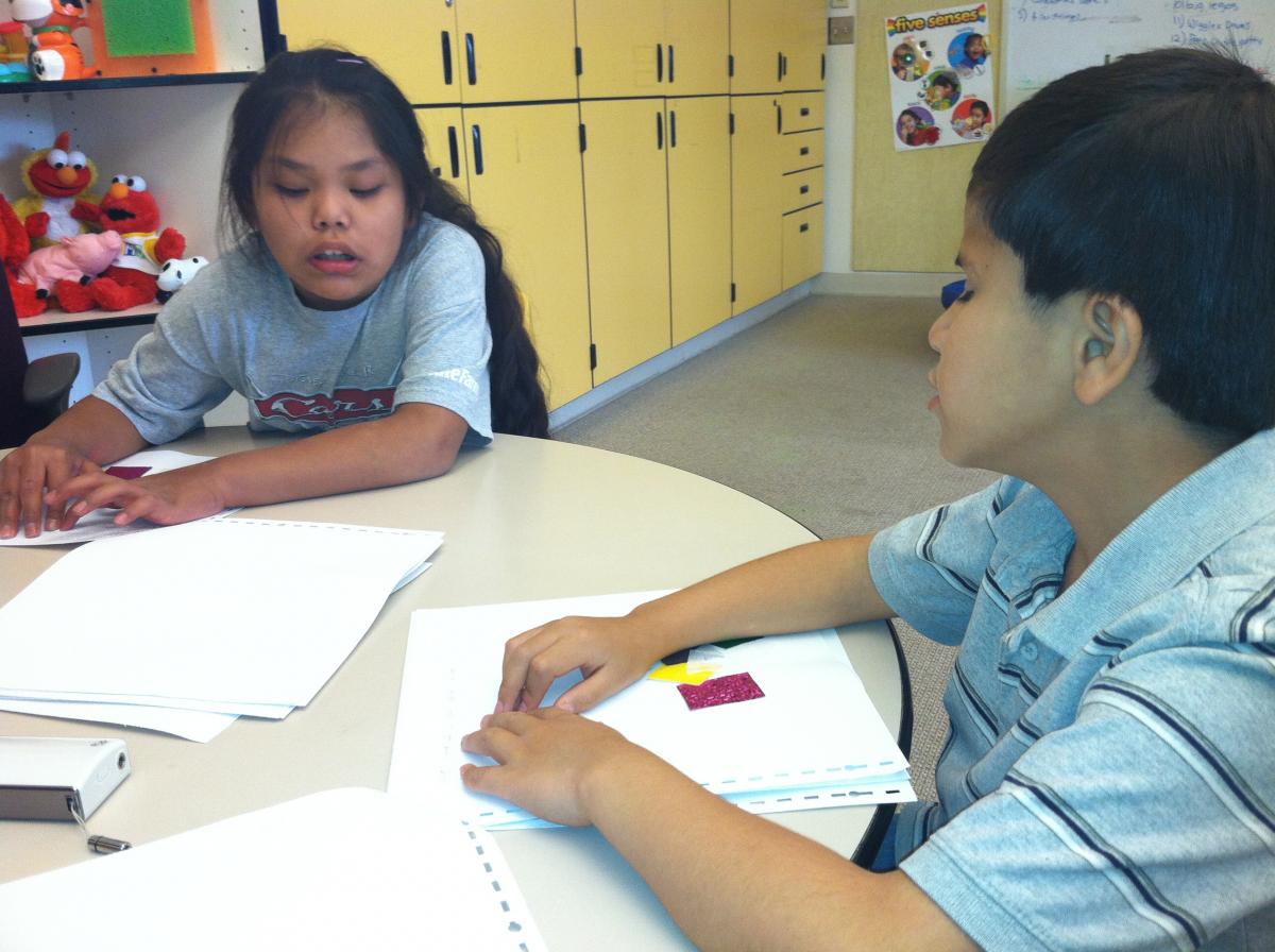 One student reads a braille story as the other listens.