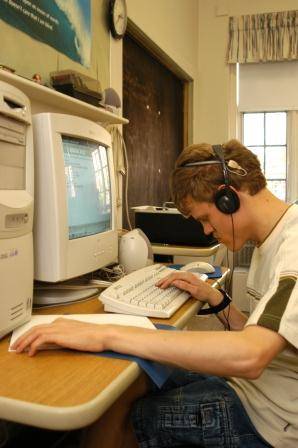 Older male student sitting at a computer using headphones and a keyboard