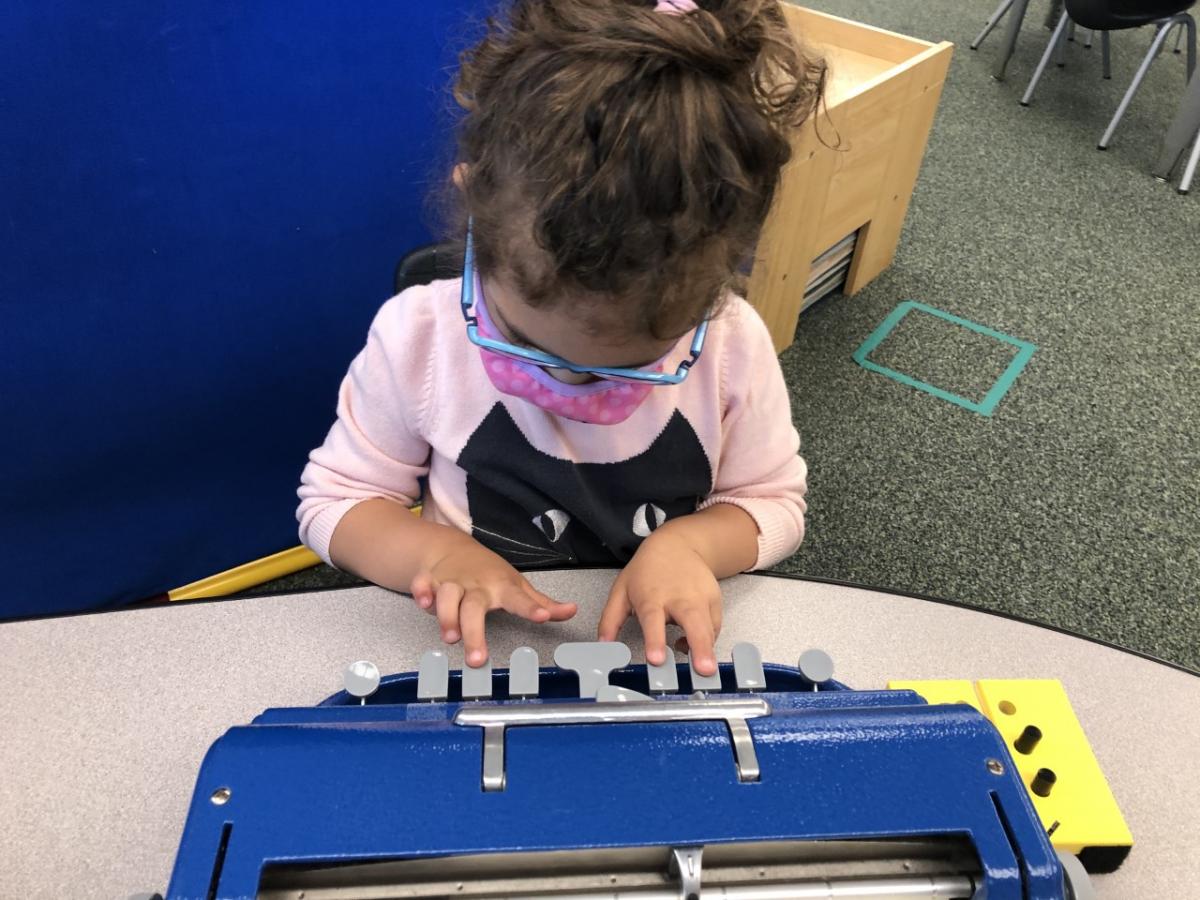 A young girl writes on a Perkins braillewriter. A young girl writes on a Perkins braillewriter.