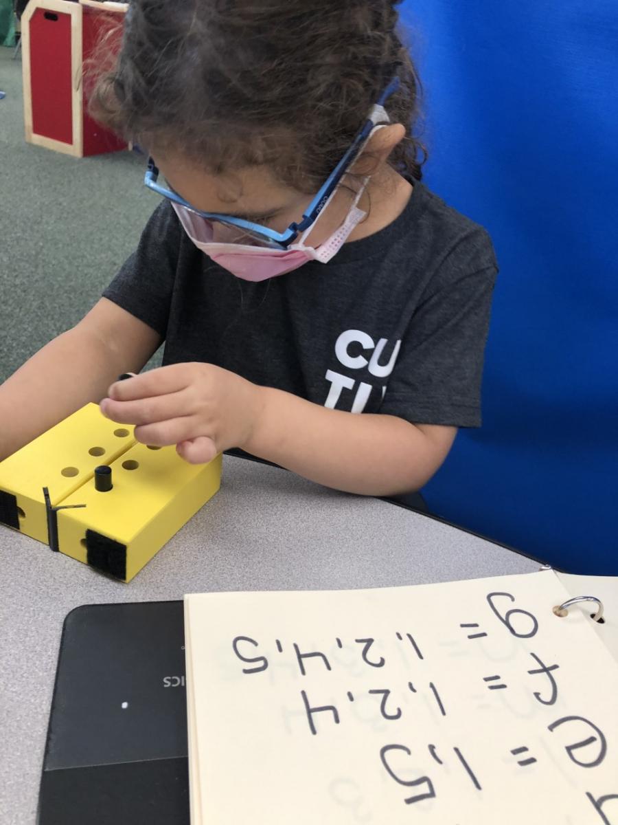 A girl uses a swing cell next to a notebook showing print letters and their corresponding dot numbers. A girl uses a swing cell next to a notebook showing print letters and their corresponding dot numbers.