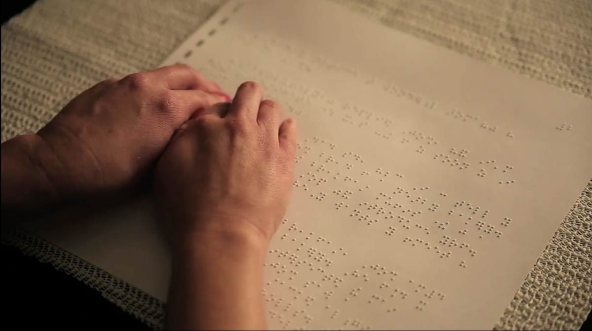 Two hands move across a page of braille text.