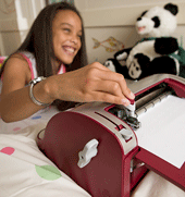 A girl writes using a Perkins braillerwriter, with Perkins Panda in the background.