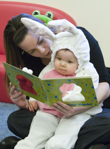 Woman reads a picture book to a toddler wearing a bunny suit.