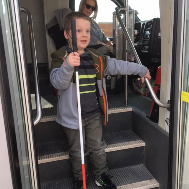 A boy holds a cane while descending the steps of the bus