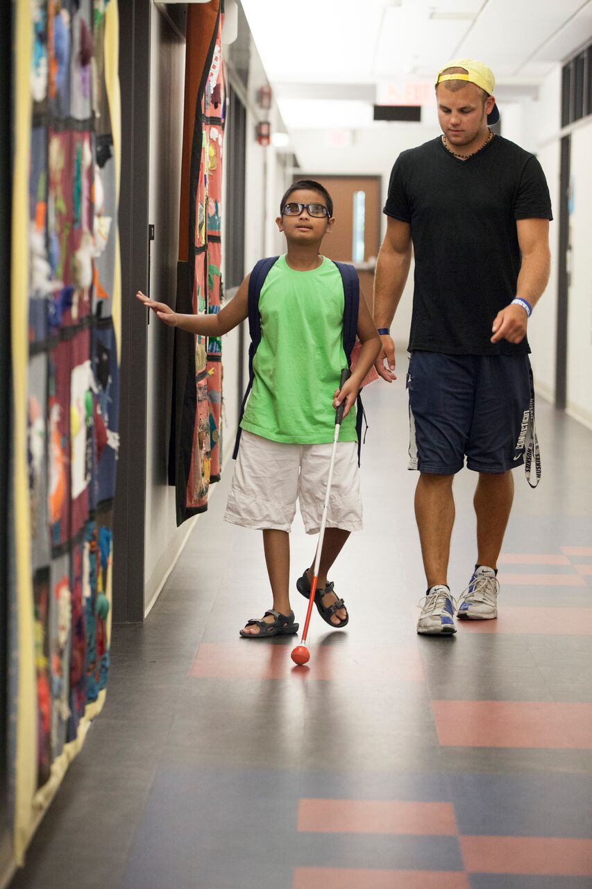 A boy travels down a school corridor using a white cane