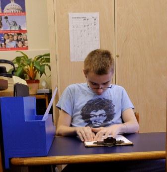 Boy wearing glasses reading braille