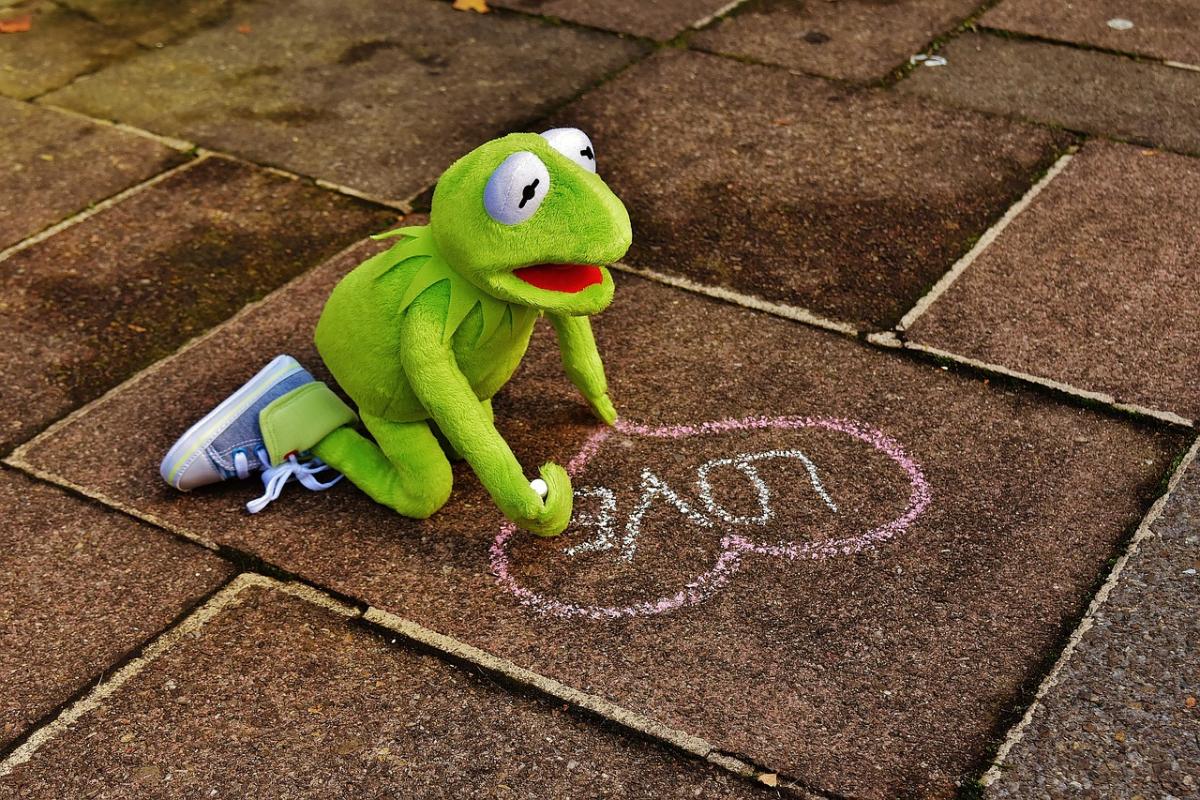 Kermit the Frog kneeling on the sidewalk and writing 