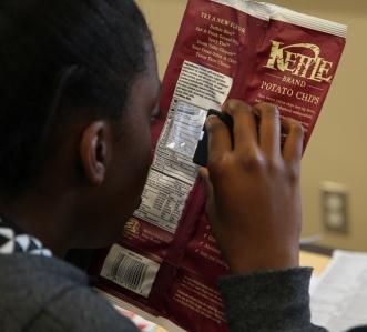Teenage girl read ingredients of a bag of potato chips using a hand-held magnifier.