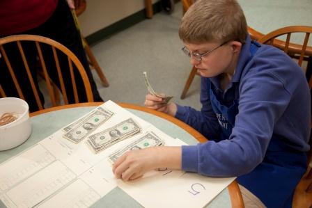Boy wearing glasses counts dollar bills and arranges them in small stacks.