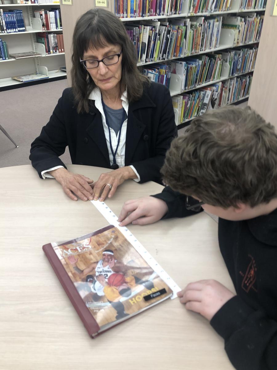 Student using ruler to measure magazine while teacher looks on