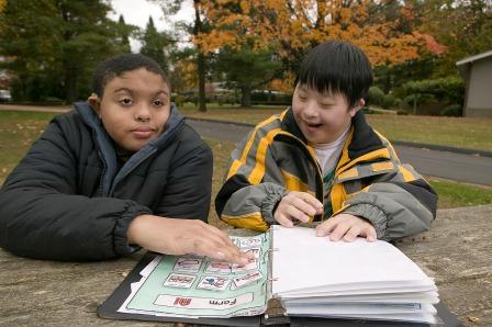 Two boys sit side by side with a book of picture symbols.