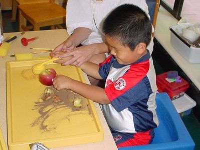 Young boy touches objects on a tray.