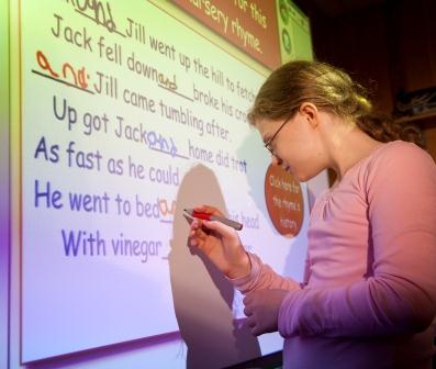 A girl wearing glasses uses a marker to write on a smart board.