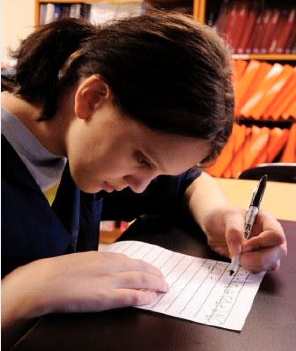 A teenage girl writes with a black Sharpie on lined paper.