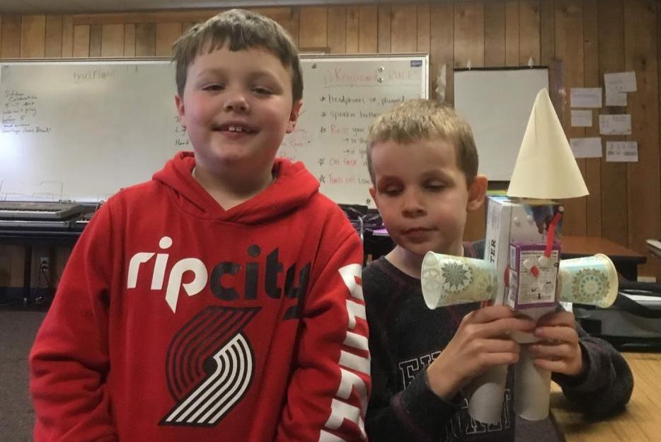 Two boys pose with the robot they created.