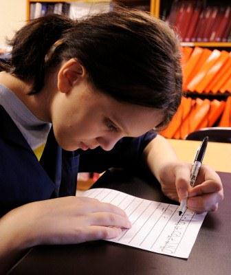 A girl with low vision uses a black marker and paper with bold lines to write.