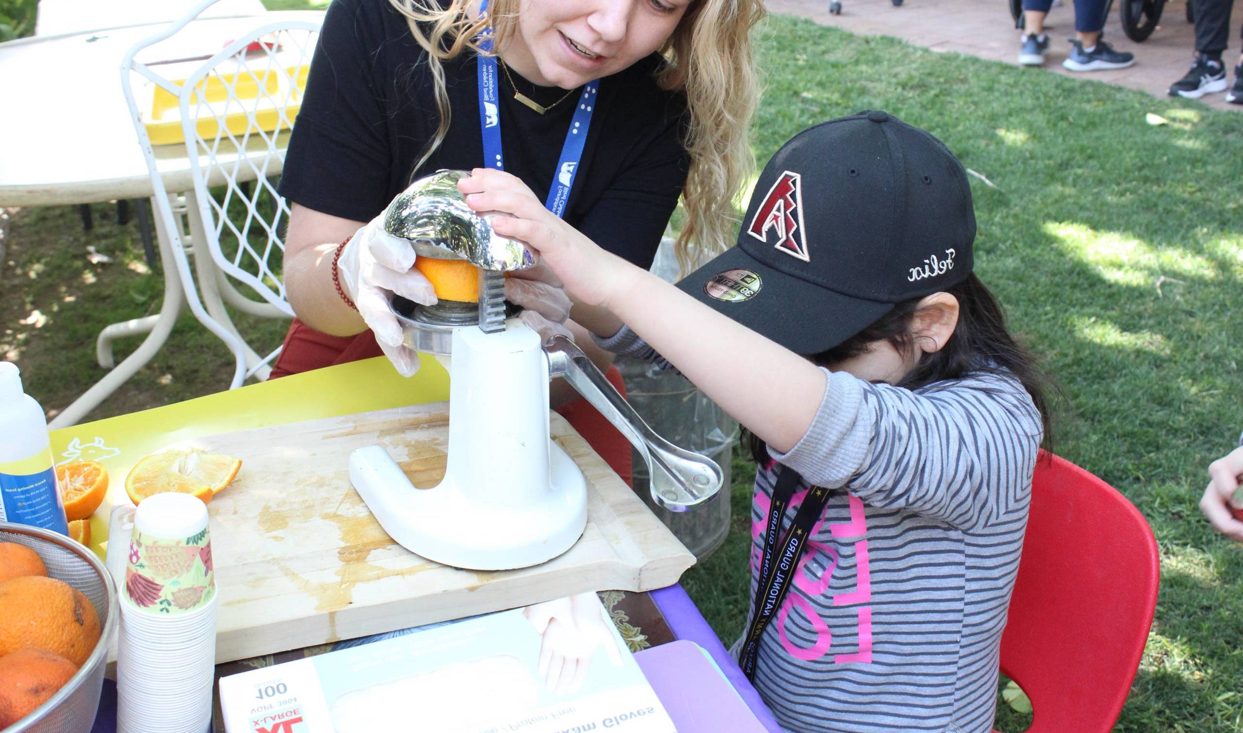 Student making orange juice with a teacher using a juicing machine.