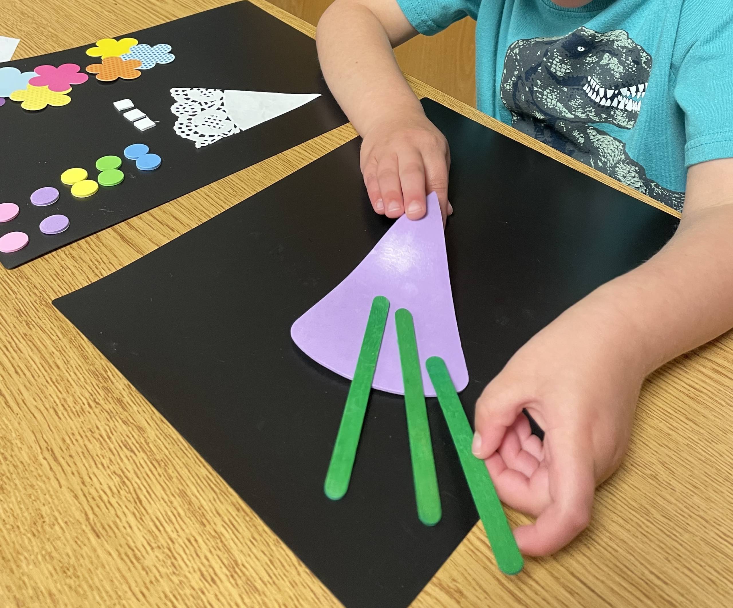 Student making a flower craft with paper, lace, textures, and popsicle sticks