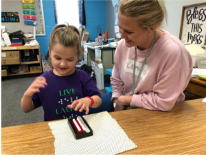 Young student using a beginners abacus with her teacher next to her.