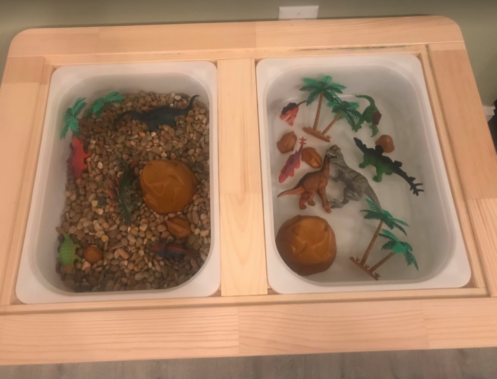 Sensory bin with plastice dinosaurs, rocks, and trees