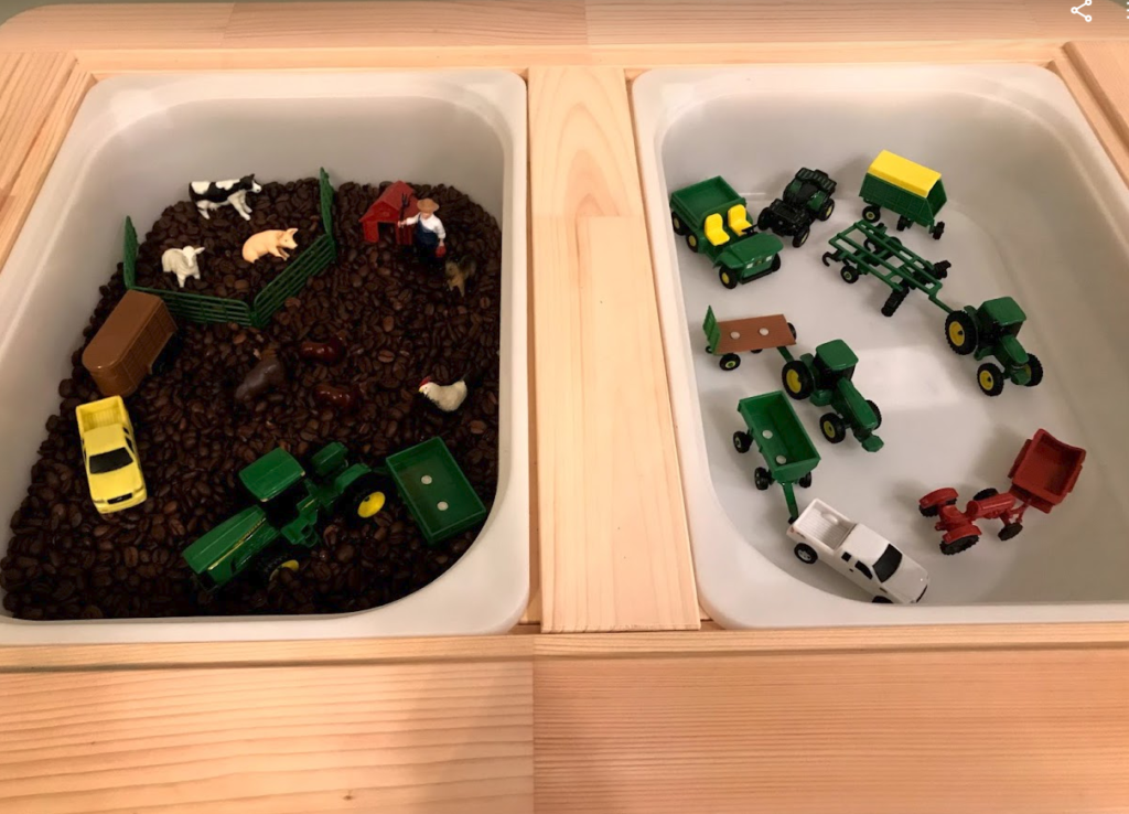 This sensory bin theme is about a farm with plastic farm animals and farm equipment, including pickup trucks. All placed in a two bin table with one having crushed coffe beans as the dirt.