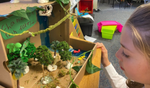 Third grade student closely viewing a rain forest scene created by her peer.