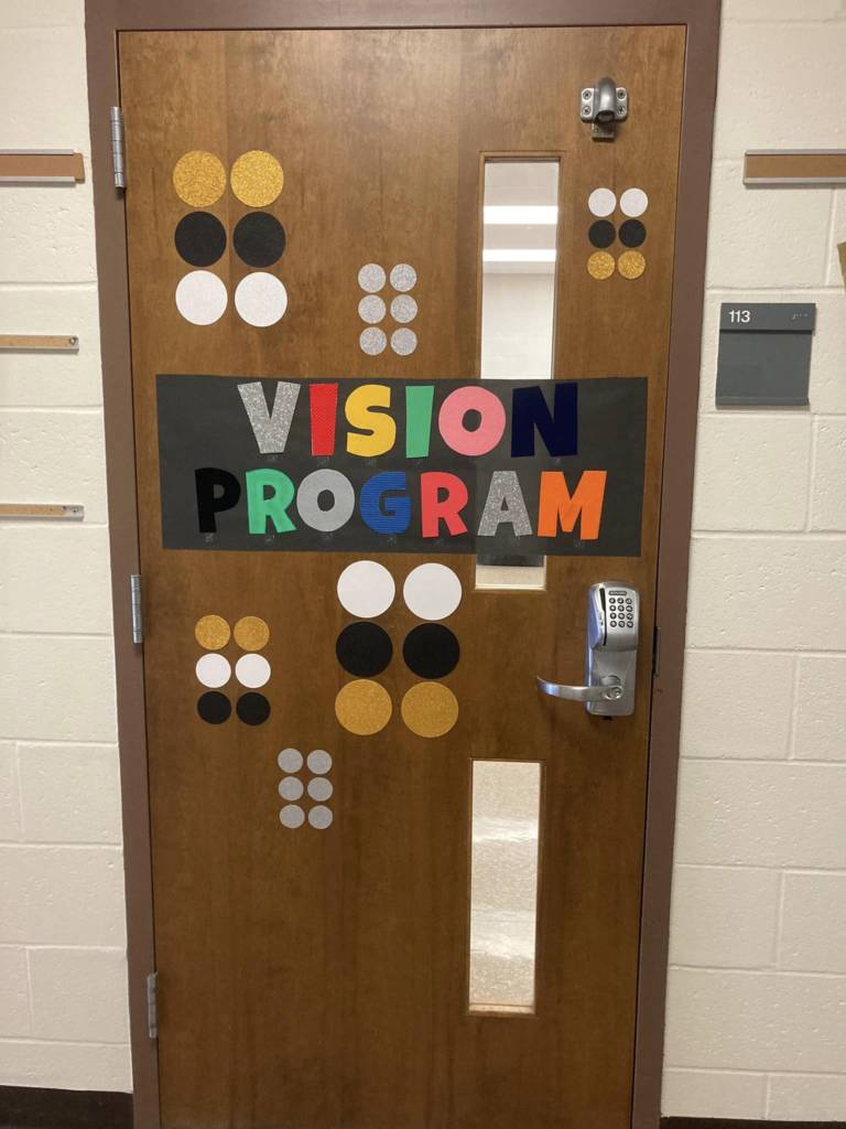 Completed door that has textured letters saying "Vision Program" and braille letters that also include large cut out circles that represent braille.