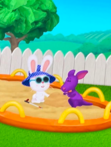 Pearl the Bunny who has glasses, a hat, and cane, playing in the sandbox with a friend.