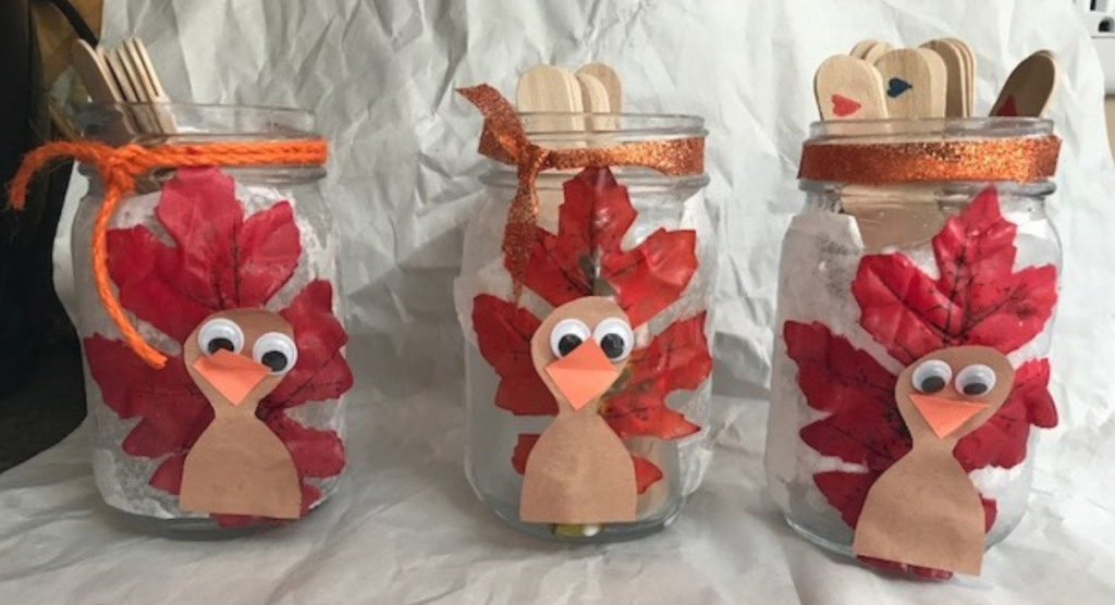 Mason Jars with a paper turkey design using a leaf as the feathers and popsicle sticks inside the jar.