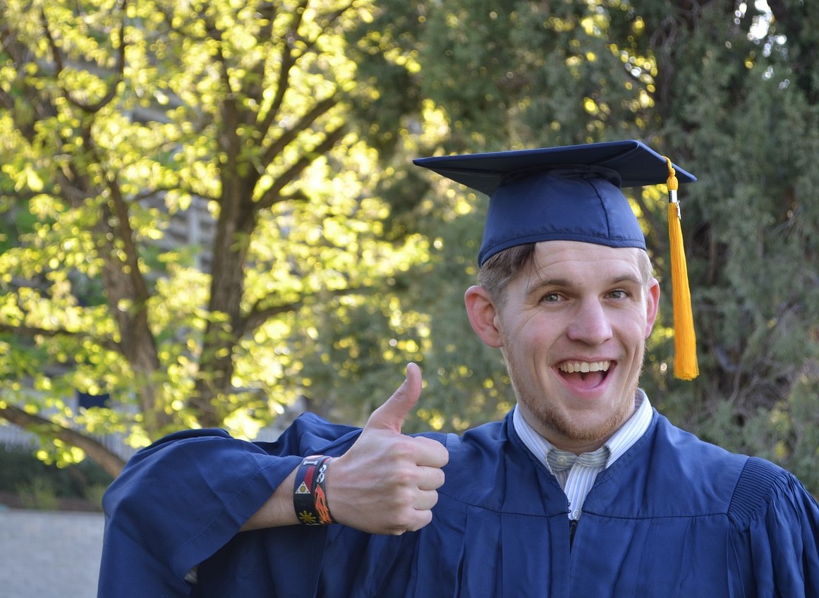 Student in a cap and gown with his thumb up and happy.