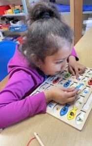Young girl matching fish puzzle pieces with the braille letters on them. 