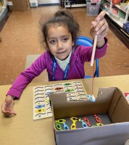 Young girl "fishing" pieces of the fish puzzle out of a box with a magnetic pole to place in the puzzle.