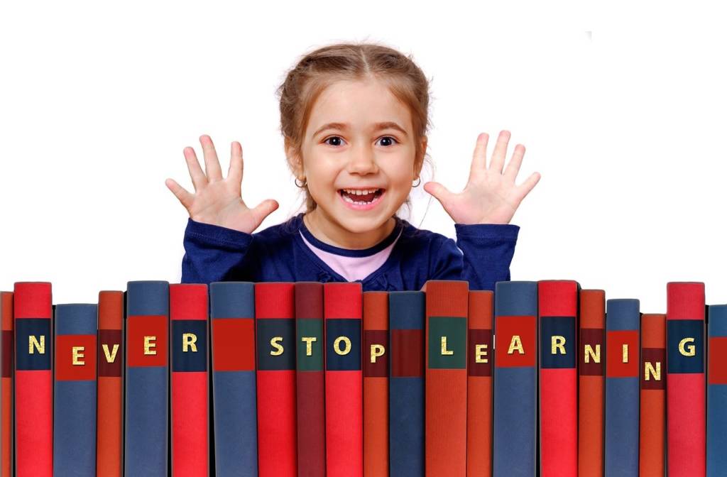 Little girl smiling with books in front of her that says, "Never Stop Learning"
