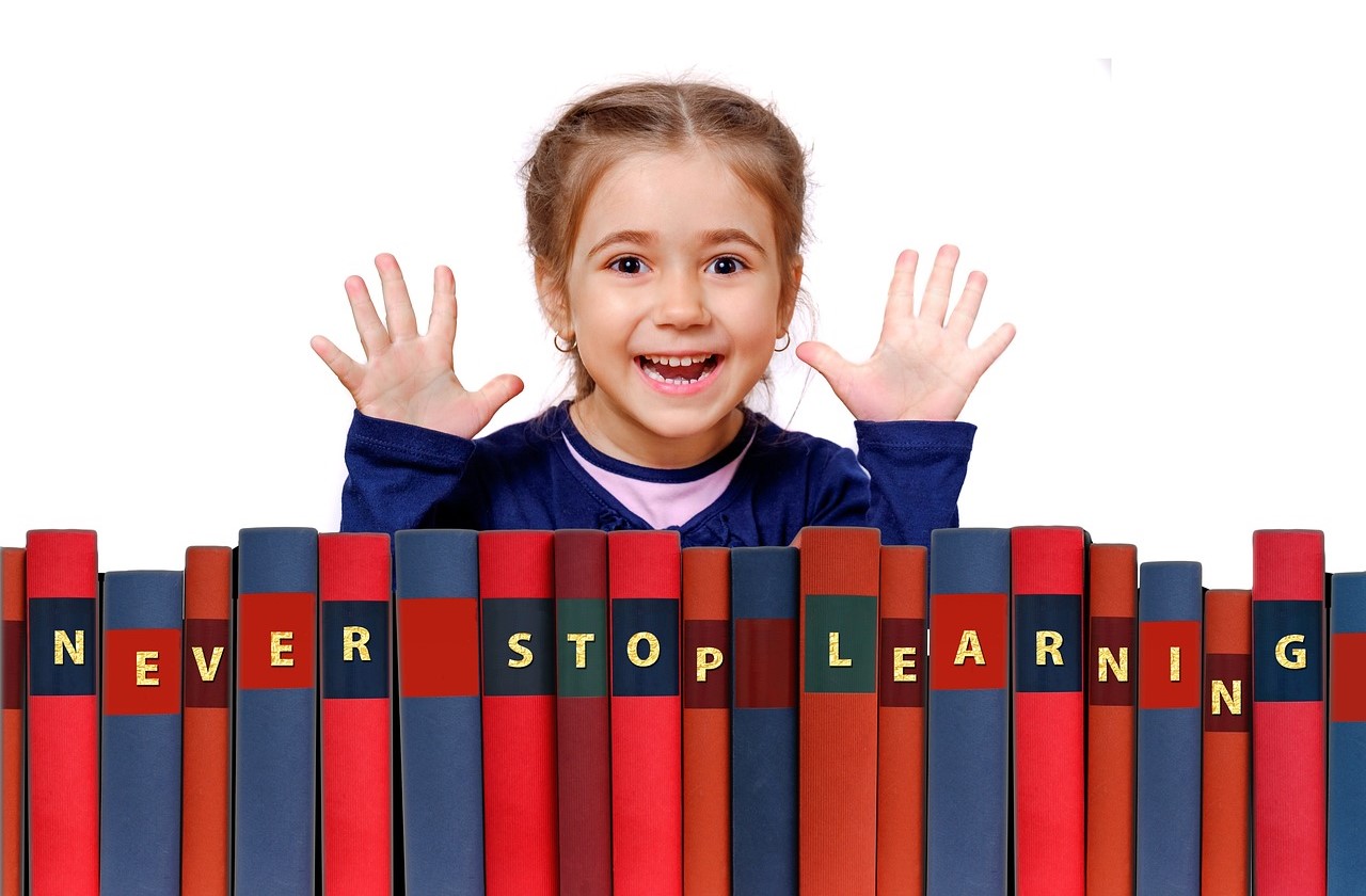 Little girl smiling with books in front of her that says, 