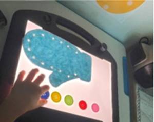 Student on a lightbox with the sewn mitten and difference colored buttons lined up next to it.