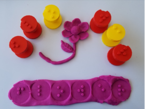 Braille play dough stampers arranged around a flower modeled in play dough and the word ‘flower’ in raised Braille letters stamped into play dough.