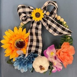 Wreath with sunflowers and other silk flowers and a ribbon on top. 