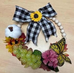 Wreath with a plastic pumpkin, grapes, butterfly, silk flowers, and ribbon on top.