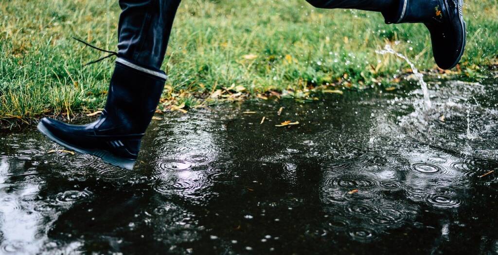 Picture of a child's legs running with rain boots on in puddles.