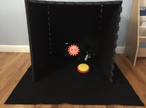 Photo of “Little Gym” that has 4 foam mats making a room with a black cloth on the floor. On the floor there is an iPad playing the Big Bang Pictures app, a Tapio connector, and yellow switch