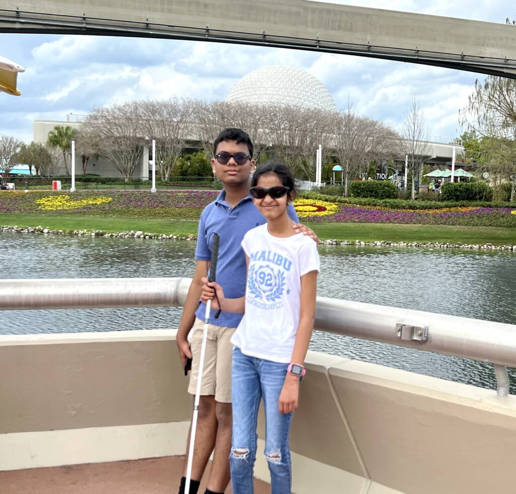 Krish standing with her brother, holding her cane, standing at Epcot.